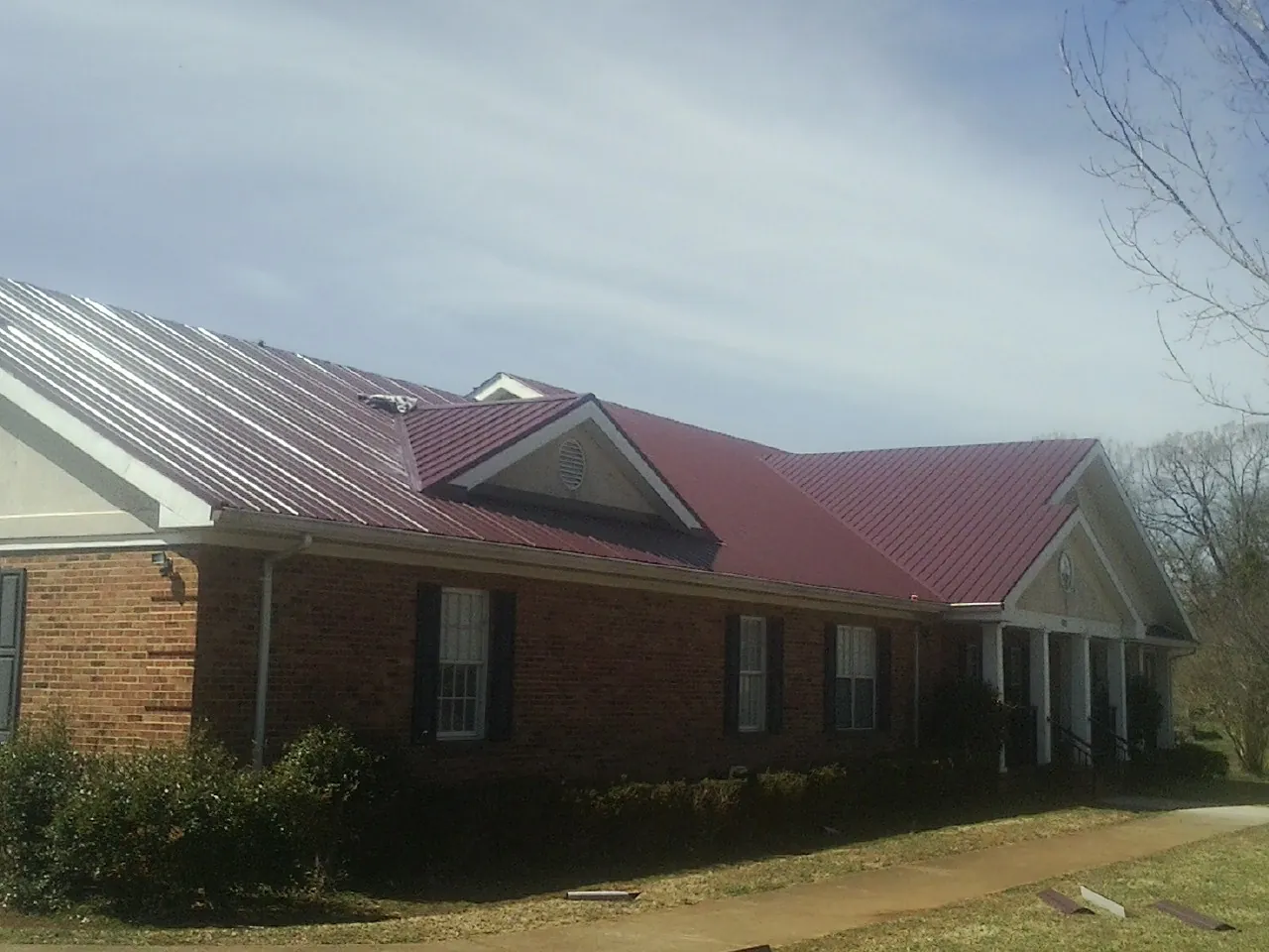 Red metal roof with gabled entries on a long brick building, from a Hail Damage Roof Repair job in Hollister