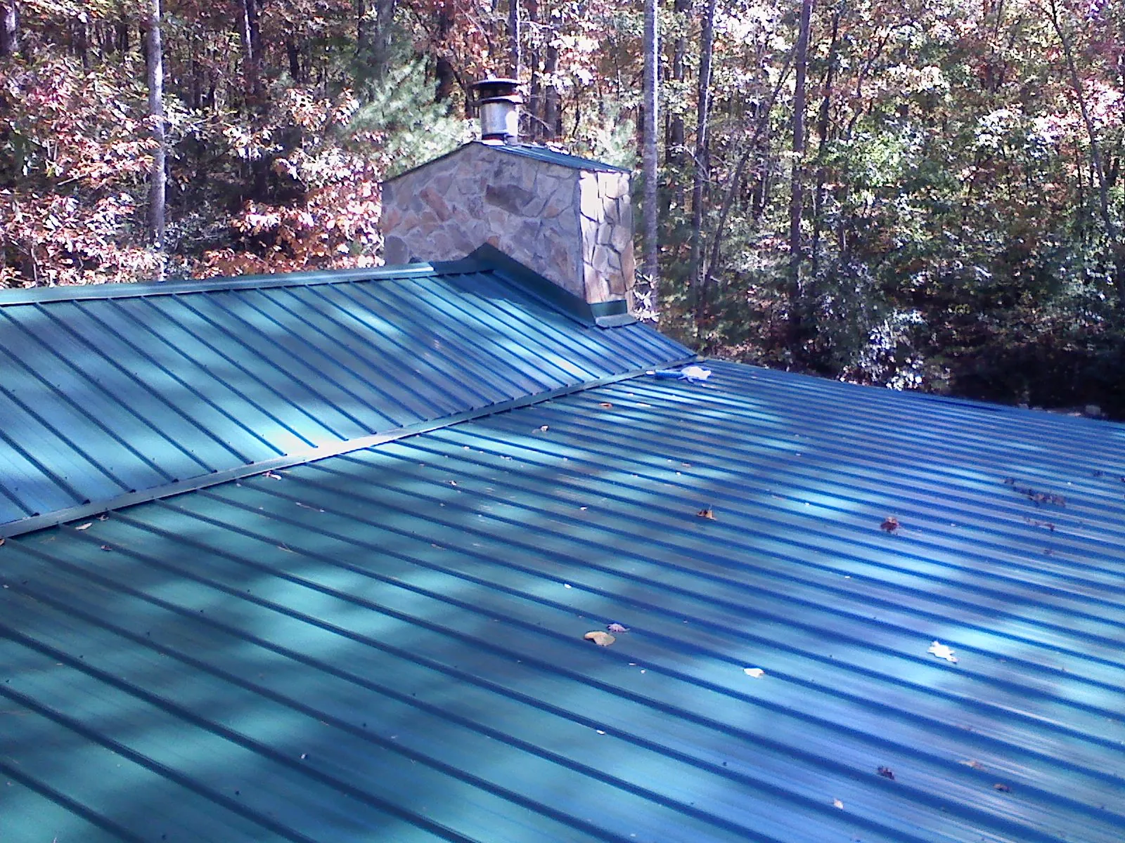 New green metal roof and stone chimney surrounded by autumn woods in Hollister