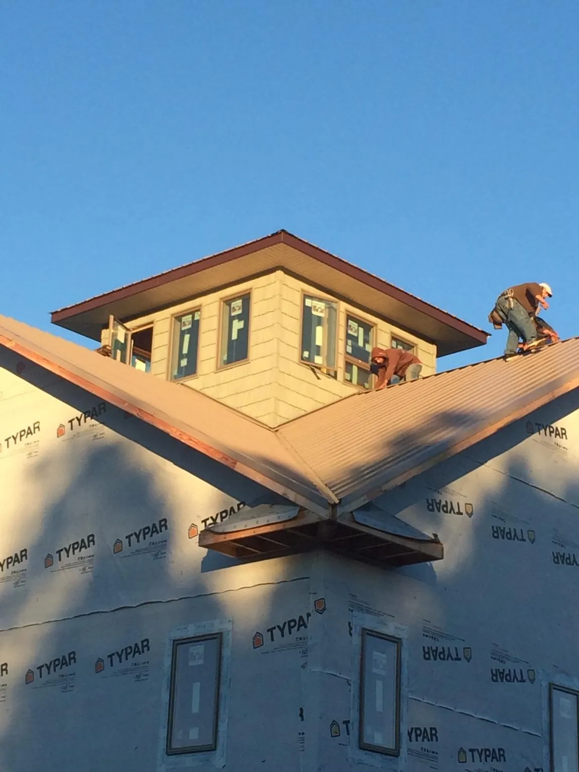 Roofers working around a rooftop cupola on a new metal roof at sunset — Roof Waterproofing in Hollister by Roofing Brothers